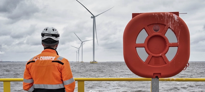 Man in safety gear looking at the sea and wind turbines