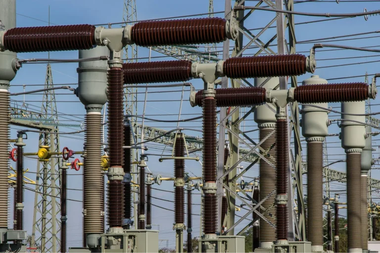 Power grid with high-voltage lines and transformers at an electricity substation under a clear blue sky