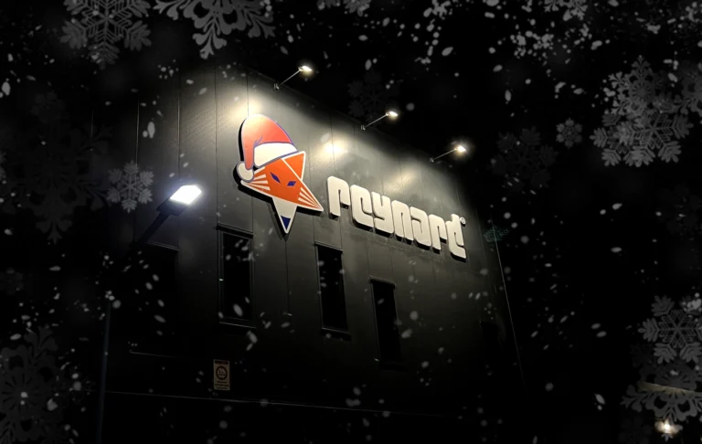 Reynard company building at night with illuminated logo featuring a festive Santa hat, surrounded by falling snowflakes and a dark wintery background.