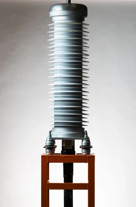 A high voltage termination component featuring a cylindrical porcelain insulator with numerous horizontal cooling fins, mounted on an orange metal support frame. The insulator has a metallic cap on top and connection points at the bottom, commonly used in electrical power transmission systems.
