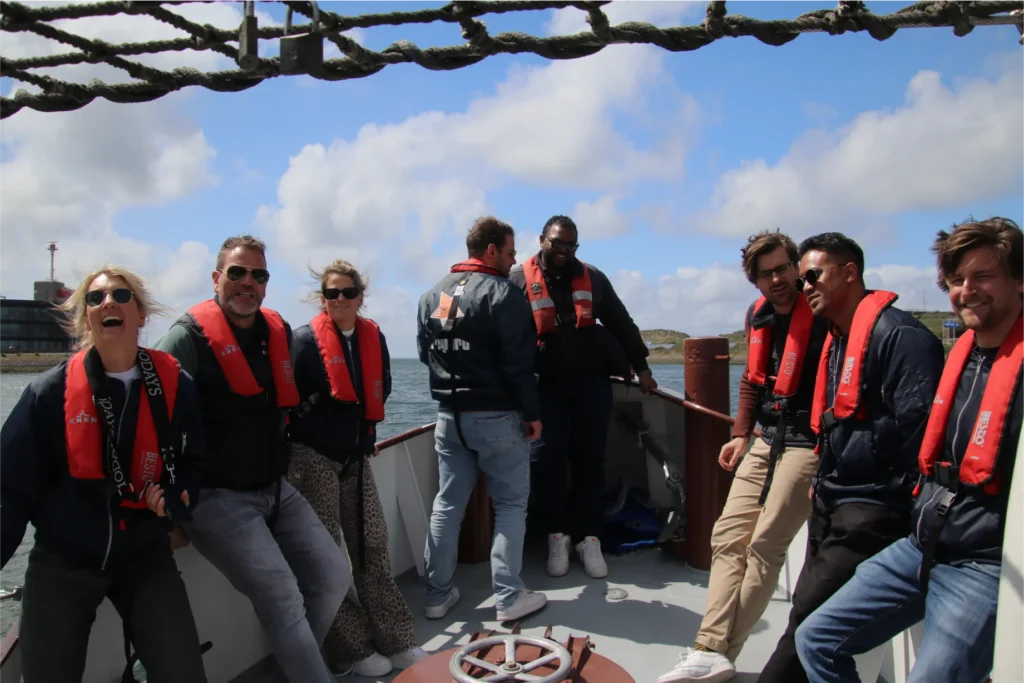 Reynard team and KNRM staff wearing red life jackets aboard KNRM rescue vessel during maritime safety demonstration, with IJmuiden port infrastructure visible in background